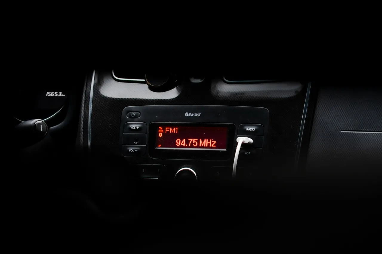 Autoradio à afficheur rouge indiquant une fréquence FM dans une planche de bord sombre, de nuit, avec un câble branché en façade